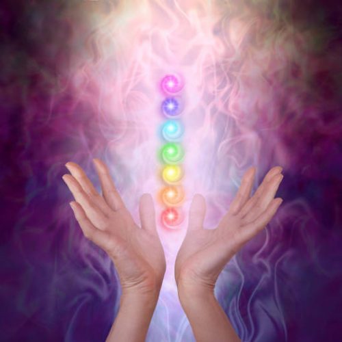 Female healer's hands either side of seven chakra vortexes on an ethereal dark to light misty swirling energy field